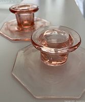 Side perspective of two pink Depression glass candlesticks showing octagonal base and candle holder top.