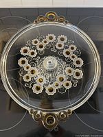 Top-down view showing the circular plate of the glass cake stand with a ring of amber-centered white flowers and amber accent handles on opposite sides.