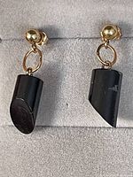 Front view of the pair of black coral drop earrings suspended from 14K gold posts and oval links in grey velvet box