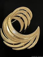 Full view of the brushed gold abstract curved crescent shaped pin showing detailed engraved textures and polished finish.