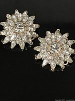 Pair of signed vintage Nina Ricci clip-on earrings arranged on a reflective black surface showing full floral design.