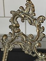 Close-up of ornate Rococo style scrollwork and floral detailing on the solid brass easel.
