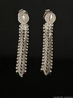 Front view of pair of long sterling silver earrings showing chevron patterned dangles with beaded edges and circular studs