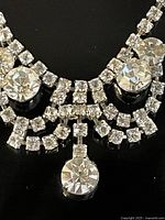 Close-up of the rhinestone lavalier necklace showing claw set larger stones and intricate smaller rhinestone detailing in silver-tone metal.