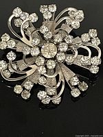 Clear stone cluster burst pin with claw settings, silver-tone metal, textured accents, and no missing stones.