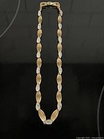 Full view of the vintage Marcel Boucher necklace showing alternating gold-toned and silver-toned micro stone set links laid flat on black surface.