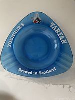 Top view of blue cobalt glass ashtray with 'YOUNGER'S TARTAN Brewed in Scotland' text and Scottish man graphic