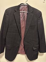 Full front view of the men's dark plaid wool suit jacket on hanger showing lapels, buttons, and flap pockets.