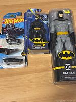 Front view of the Batman toy lot including Hot Wheels cars and Batman figures in packaging on a wooden surface.