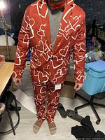 Man wearing a red suit with white heart and arrow prints with matching pants and red bow tie, showing the detailed pattern and fit of the suit.