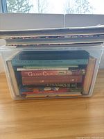 Side view of plastic bin with visible book titles including Morocco travel guide, The Golden Calm, and The Private Capital.