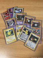 Lot of 14 assorted Pokemon cards laid out on a wooden surface, including Pikachu, Unown, Lugia, Ho-Oh and others in protective sleeves.