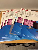 Six sealed 3M High Clarity Privacy Screen Protector packages laid out on a wooden surface showing front packaging design.