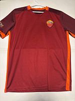 Full front view of maroon AS Roma football jersey with orange details on sides, collar and sleeve Ends.
