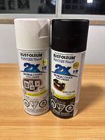 Two Rust-Oleum Painter's Touch 2X Ultra Cover spray paint cans, one flat white and one semi-gloss black, shown side by side.