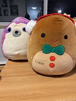 Photo of two Squishmallow plush toys: a purple sloth and a brown gingerbread man named Liam