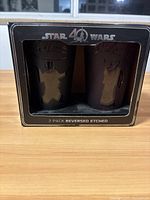 Front view showing two etched glasses featuring Yoda and Darth Vader designs in a black box with Star Wars 40th logo and text indicating 2 pack reversed etched glasses.