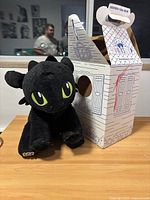Front view of Toothless plush sitting next to the decorative box with a house design.