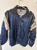 Vintage Kappa windbreaker jacket hanging, showing front view with zipper closed and logo on chest and sleeves.