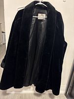 Full view of the black vintage faux fur coat displayed on a hanger, showing the plush texture and smooth lining.