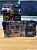 Stacked boxes of Warhammer 40,000 miniatures including Combat Patrol, Imperial Guard Cadian Shock Troops, Knight Armiger, and Cadian Infantry Squad. Display of box art and titles.