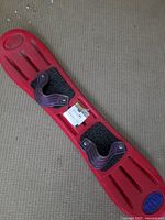 Photo of red Riva Parabolix 43 inch snowboard showing top surface with attached purple bindings and black grip pads.