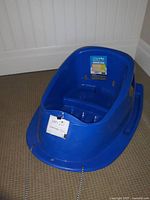 Blue baby sled with molded seat, footrests, handles, and pull rope, positioned on carpeted floor.
