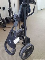 Folded Butler Golf 3 wheel golf cart standing on floor showing front and side profile with visible dirt and wear on wheels and frame.