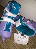 Pair of purple and teal Disney Princess adjustable ice skates shown at an angle, highlighting white straps and worn condition.