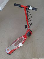 Red Razor electric scooter standing upright on carpet, showing the deck, handlebars, and wiring.