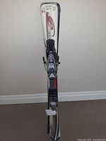 Pair of Rossignol EDGE JR. junior skis with bindings shown upright against wall, white base with red and black graphics, some wear visible.