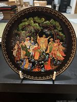 Front side of the decorative plate showing the Russian folklore scene under a gold patterned border on black background.