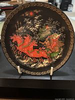 Front view of the decorative plate showing hand-painted winter scene with woman in sleigh drawn by red horses and gold ornamental border.