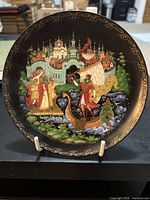 Front view of the decorative plate showing a colorful Russian folklore scene with castle, characters, and boat.