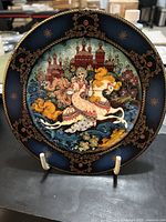 Front of decorative Russian Seasons collector plate showing detailed artwork of woman on horse with Russian buildings in background and floral patterns.