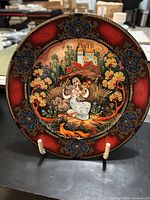 Front view of the decorative plate showing a traditional Russian folk art scene with a woman, wheat, and a church in the background, bordered with red and gold ornamental patterns.
