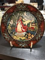 Front view of the porcelain plate showing detailed autumn-themed artwork of a woman in traditional costume and a village landscape.