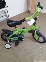 Green children's bike with Teenage Mutant Ninja Turtles Half Shell Heroes stickers, black seat, tires, and training wheels shown from side angle.