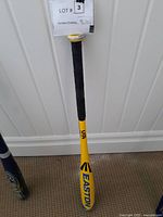 Yellow Easton baseball bat with black grip leaning against a white wall showing branding and condition.
