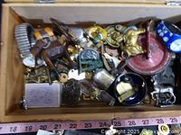 Top view showing the wooden jewelry box filled with assorted small items including metal objects and a watch band, with measuring tape for scale.