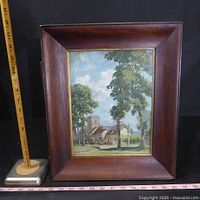 Front view of framed painting depicting an English village scene with church and trees in a wooden frame with gold trim