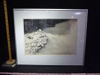 Front view of the framed black and white artwork of a rocky stream with measuring tapes for scale.