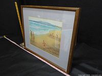 Side view of the framed beach scene painting showing the wooden frame and matting.