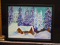 Frontal view of framed painting showing a snowy winter cabin and trees scene with visible signature LB on bottom right corner.