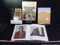 Photo of three large art books including Toulouse Lautrec and others. The open book shows painted portraits.