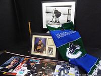 Overview photo showing magazines, framed photo, and Canucks jersey/scarf on black background