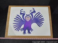 White paper serigraph print of a purple stylized bird with two heads and multicolor patterned center, laid on wooden board with measuring tape