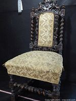 Full view of Gothic Revival carved wooden chair with detailed upholstery showing wear on seat fabric and twisted spindle legs.