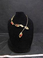 Front view of the necklace displayed on a black necklace bust with a black backdrop. The necklace has leaf-shaped brutalist bronze elements with red stones.