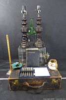 Photo showing the table lamps, glass vase, leather case with flatware, old book, ceramic owl and decorative picks arranged together